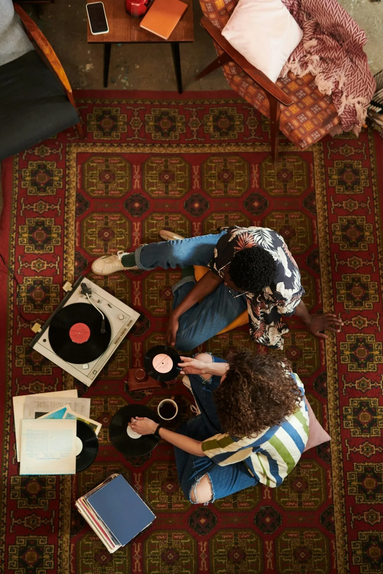 Overview of young intercultural couple sitting on red carpet in living room